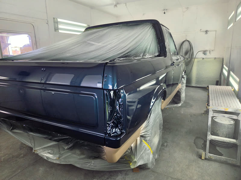 A pickup body freshly painted deep green, still masked with plastic and paper, standing in a spray booth.