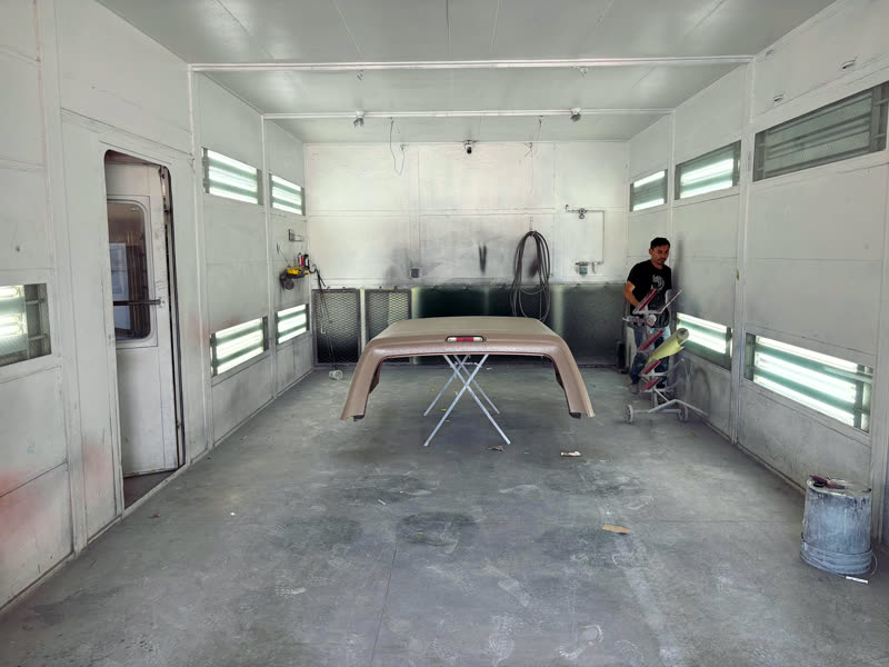 Inside the spray booth: a bonnet in primer on a stand, and someone working at the far wall.