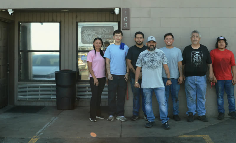 Seven people standing together outside the shop, along the wall beside the door marked 103.