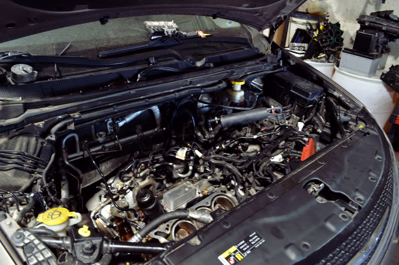 An engine bay from above with the cover off, intake and wiring exposed.