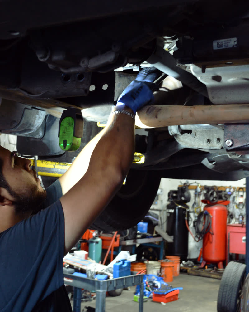 A technician in blue gloves reaching up into the underside of a car on the lift.