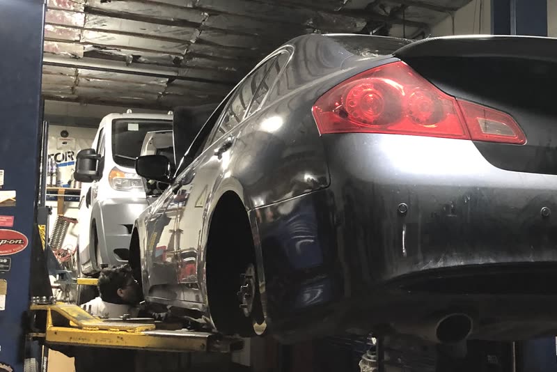 Inside the bay: a car raised on a two-post lift with its wheels off, a technician working underneath it, and a second car on the next lift.