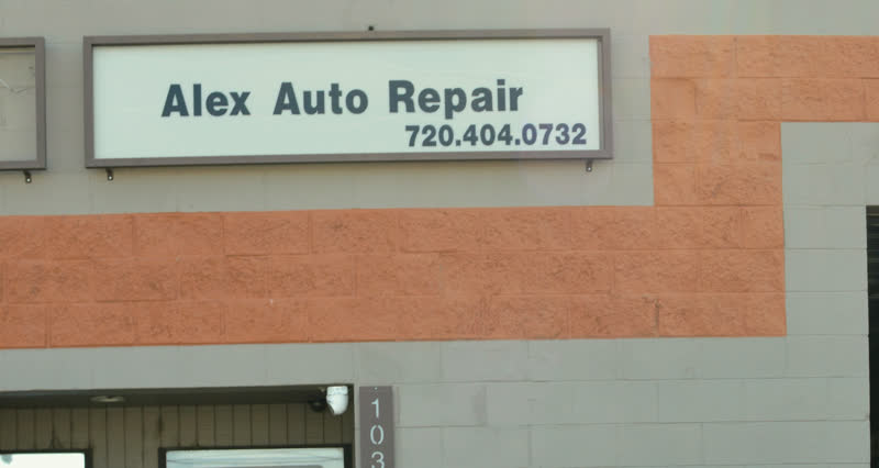 The illuminated sign on the building reading “Alex Auto Repair, 720.404.0732”, the terracotta band running beneath it.