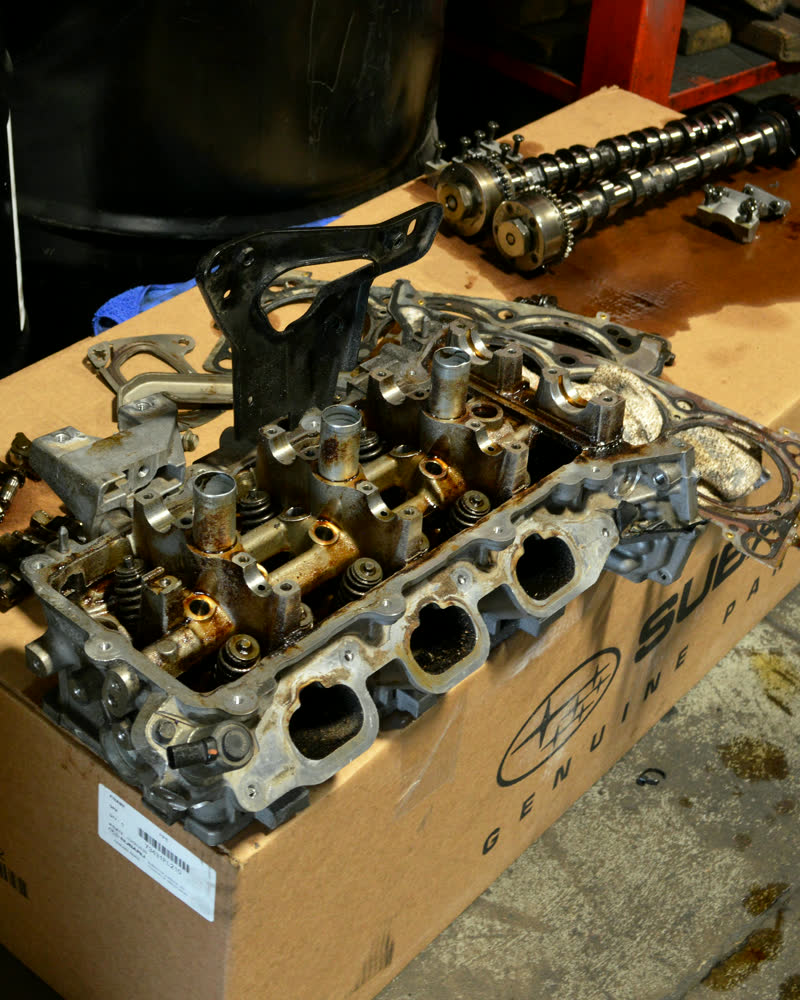 A cylinder head and camshaft lifted out and laid in a box on the shop floor, valve gear and bolts visible.